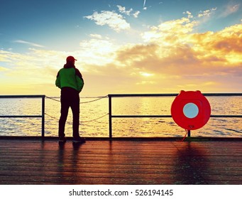 Man Stand At Handrail On Mole And Looking Over Sea To Morning Horizon. Sunny Blue Sky, Smooth Water Level