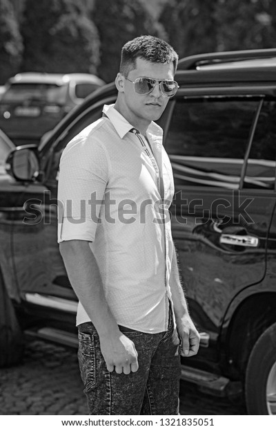 Man stand near car on city\
street. Businessman in stylish sunglasses on sunny outdoor. Driver\
at automobile transport. Travelling and transportation\
concept.
