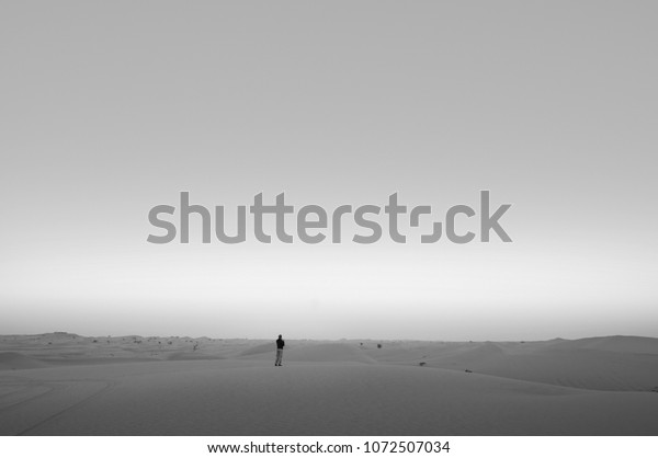 A man standing alone in empty Al Wathba desert. Abu\
Dhabi, United Arab Emirates in evening or morning. Black and white\
image