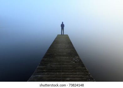 Man standing alone on the end of a jetty, looking into the fog.
