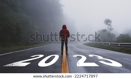 Man standing alone on the road and looking at target with text 2023 written on the road in the middle of asphalt road with at sunset. Concept of planning, goal, challenge, new year resolution.