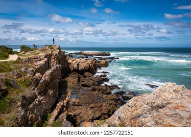 A man standing alone on rocky cliffs along the Cliff Path looking out to Walker Bay and the ocean waves. Hermanus, Whale Coast, Overberg, Western Cape, South Africa. - Powered by Shutterstock