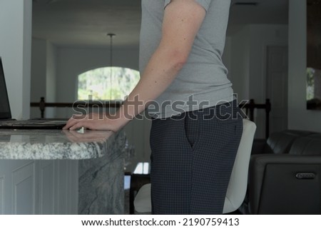 Man standing with anterior pelvic tilt posture. This man has his hands on a table.