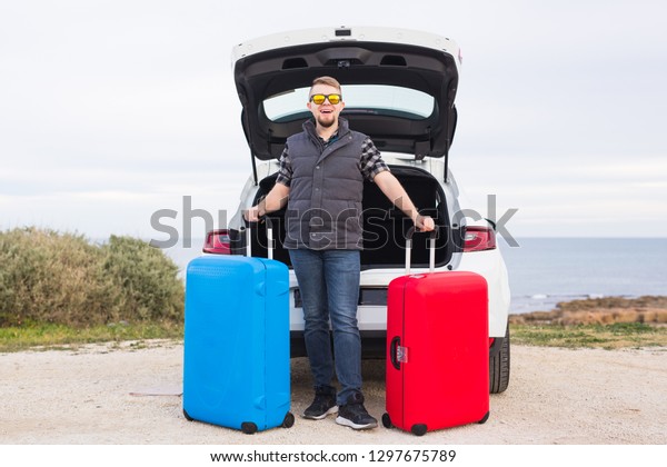 Man standing in back of car smiling and getting\
ready to go. Young laughing mle standing near open trunk of a car.\
Summer road trip