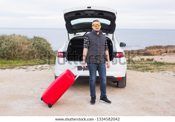 Man standing in back of car smiling and getting\
ready to go. Young laughing mle standing near open trunk of a car.\
Summer road trip