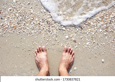 The man standing barefoot on the beach with White bubbles and many shells.