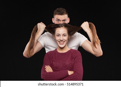 Man Standing Behind A Woman And Holding Her Hair  Like Mustaches On Black Background 