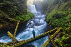 Man Standing By A Koosah Falls, Also Known As Middle Falls, Is Second Of The Three Major Waterfalls Of The McKenzie River, In The Heart Of The Willamette National Forest, In The U.S. State Of Oregon. 