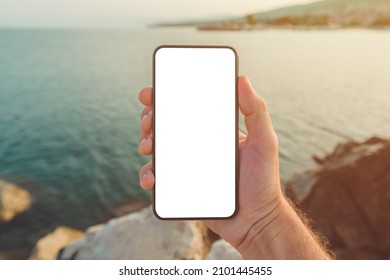 Man Standing By The Sea And Holding Mobile Smart Phone With Blank Mockup Screen, Closeup Of Hand And Device, Selective Focus