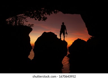 Man standing with a camera in front of a limestone cave by the sea at sunset, Photographer in front of the cave