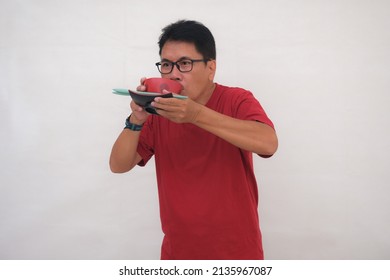 Man Standing With Casual Clothes, Sipping Soup From Red Bowl In His Hands