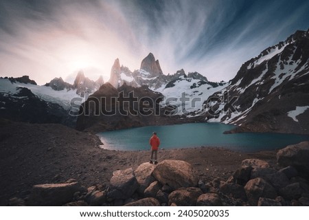 A man standing in the cliff with Mt.fitzroy as background, beautiful sunset and river in Laguna de Los Tres (Patagonia, El chalten, Argentina)