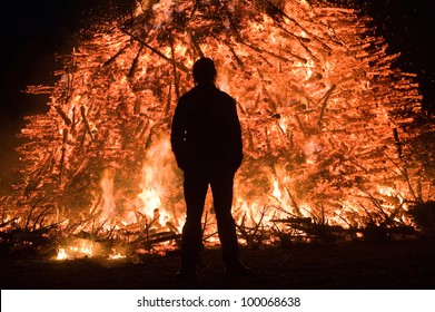 A man is standing close at a huge bonfire, a tradition with easter in Nort-West Europe.