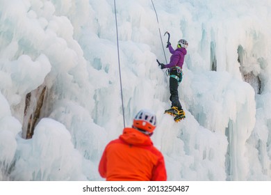 Man standing and controlling a safety top rope while female with ice climbing equipment, climbing on a frozen waterfall - Powered by Shutterstock