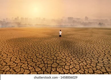 A Man Standing At Empty Land Of Dry Cracked Earth And Looking To The Big City With Air Polluted Environment Metaphor Climate Change, Water Crisis, Environment Pollution Of Activity From Urban Concept.