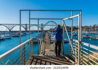 Man standing at the entrance of boat ramp docks and the Yaquina Bridge in Newport Oregon in the background.