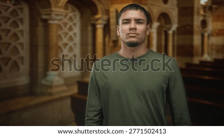 Man standing, face forward looking at camera with neutral expression in a church nave between wooden pews and stone arches; quiet introspection.
