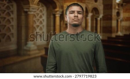 Man standing, face forward looking at camera with neutral expression in a church nave between wooden pews and stone arches; quiet introspection.