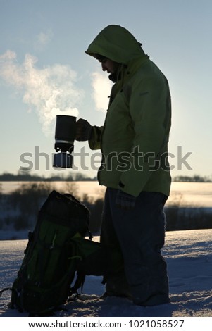 Man standing at the field in winter. He is going to drink hot coffee outside. Backlighting. Closeup. Silhouette