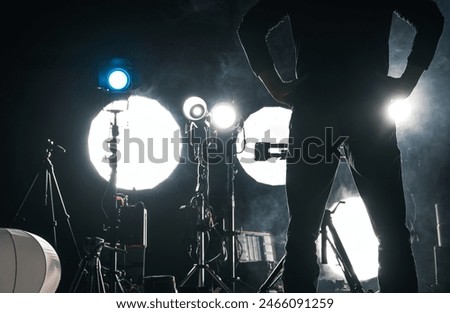 A man is standing in front of a camera in a dimly lit room recording movie or taking a photograph.
