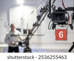 A man is standing in front of a camera with a number 6 on it. The camera is being operated by a remote control. The scene appears to be a film set