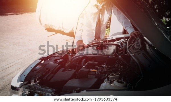 A man standing in\
front of a car with a bonnet Overlooking the engine room and trying\
to fix it his self.