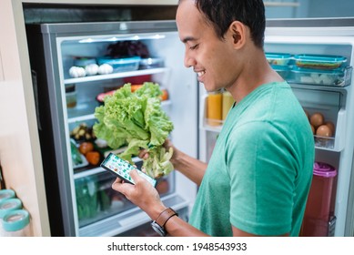man standing in front of the fridge while holding his mobile phone