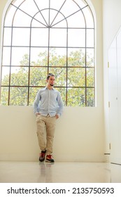 A man standing in front of a large window with natural light and greenery
