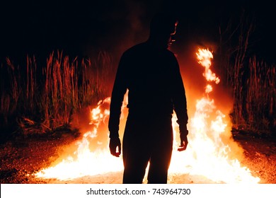 Man standing in front of the line of fire. Silhouette of the man in front of camp fire. Atmosphere of the forest. - Powered by Shutterstock