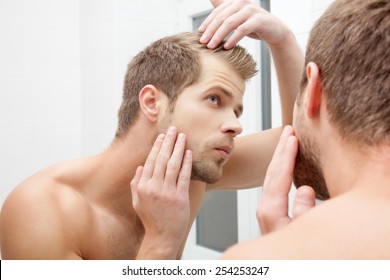 Man Standing In Front Of Mirror, Worrying About Hair Loss