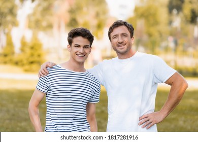 Man Standing With Hand On Hip And Hugging Teenager Son Outside