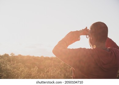 Man Standing In High Grass And Looking Into The Distance His Hand Covering Eyes From Bright Sunset Sun. Exploring Concept