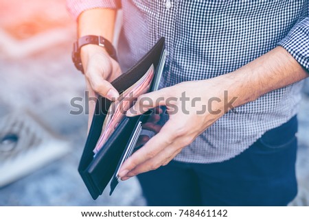 Man standing holding black wallet full of money
