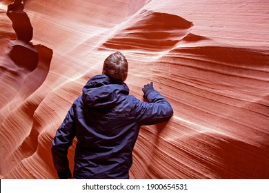 Man standing inside beautiful Antelope slot canyon, Page, Arizona. Guy with gloves and winter jacket hiking through narrow pathways in between smooth sand stone formations.