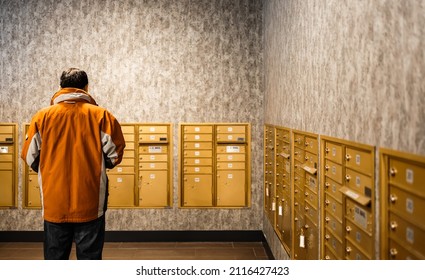 Man Standing At Mailroom Inside Apartment, Depth Of Field. People Waiting For Getting Letter At Letterbox. Mailman Or Receiver Concept, Deliver Or Receive Mail From Metal Storage By Room Number.