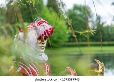 A man standing in mask and red masquerade costume agains the pond background