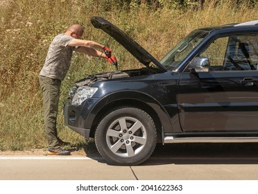Man standing with mechanic tool near car with hood up outdoors in summer and repairing it after car break up in trip.