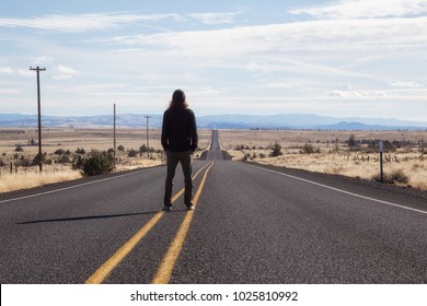 Man Is Standing In The Middle Of The Long Road During A Vibrant Sunny Day. Taken In Oregon, North America.