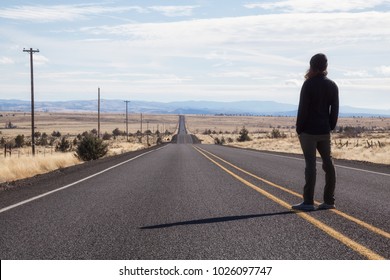 Man Is Standing In The Middle Of The Long Road During A Vibrant Sunny Day. Taken In Oregon, North America.