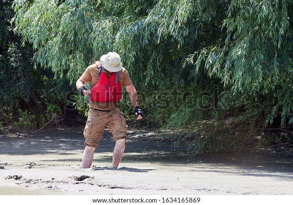 Man standing in\
natural quicksand river, clay sediments, sinking, drowning quick\
sand, stuck in the soil