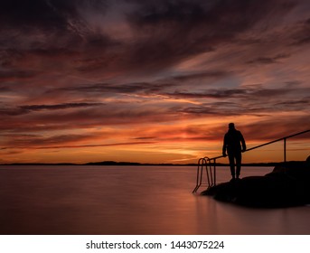 A Man Standing Near The Ocean With A Swimming Ladder By His Side. Taken With A Slow Shutter Speed To Give The Water A Smooth Look.