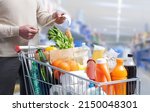 Man standing next to a full shopping cart and checking the grocery receipt