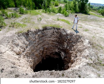 A man standing next to a huge sinkhole. Hole's bottom is not visible, as it's very deep