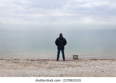Man standing on the beach by the water, alone, looking into the distant horizon  - Powered by Shutterstock