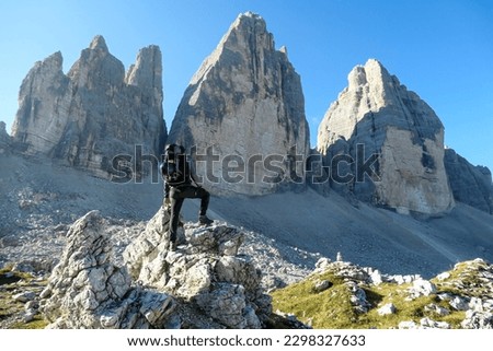A man standing on a big boulder and enjoying the close up view on the Tre Cime di Lavaredo (Drei Zinnen), mountains in Italian Dolomites. Sharp and high mountain wall. Desolated and raw landscape