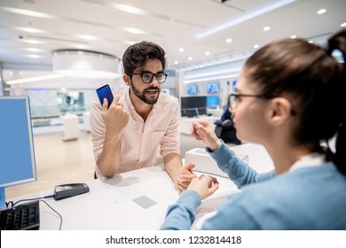 Man Standing On Cashier And Complaining For New Smart Phone While Worker Listening To Him. Tech Store Interior.