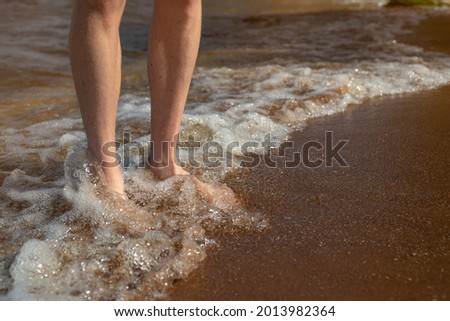 A man standing on the clean sandy beach with wave motion coming to the feet. Selective focus.