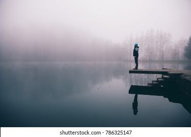 Man standing on a deck above a misty lake