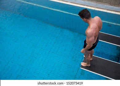 Man Standing On Diving Board At Public Swimming Pool Above The Water