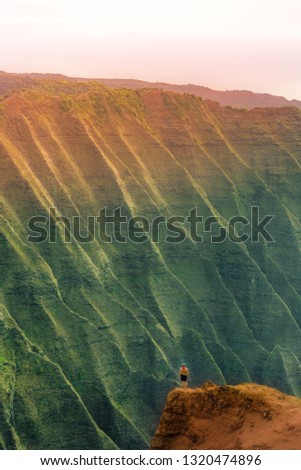 Man Standing on the edge of a cliff and enjoys the sunset on Hawaii, Kauai, Na pali coast.